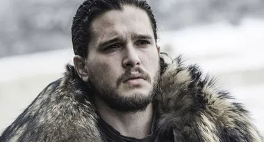 A man with a beard and dark hair wearing a fur cloak looks serious against a snowy background.