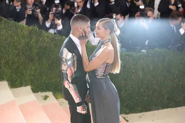 A couple poses on Met Gala steps, with photographers capturing their metallic-themed outfits.