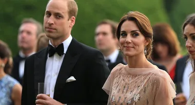 Elegant couple at an outdoor formal event; man in a tuxedo, woman in a shimmering dress, surrounded by people.