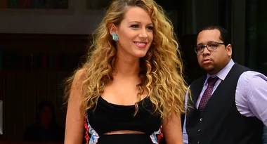 ```plaintext
Woman in a black dress with long, wavy hair smiling, standing outdoors.
```