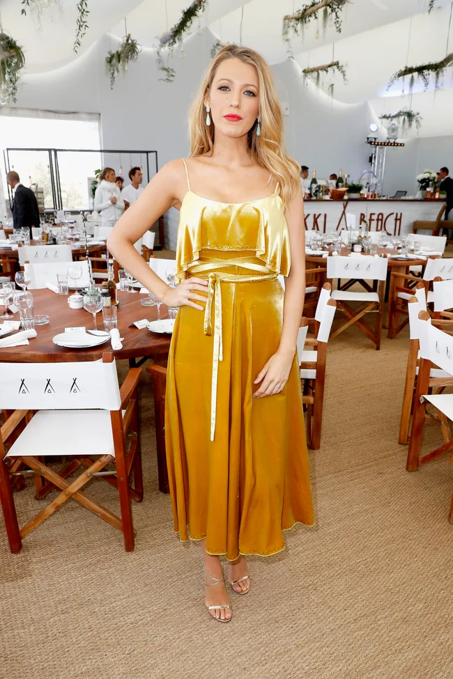 A woman in a yellow dress poses in a decorated dining area with wooden tables and white chairs.