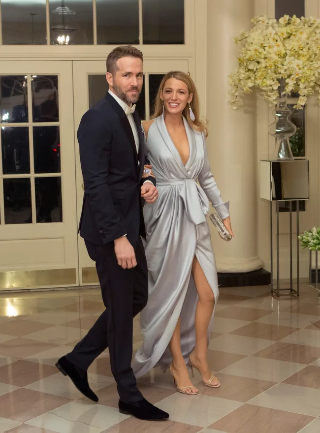 A couple in formal attire walking inside a venue, with woman in a silver gown and man in a black tuxedo.