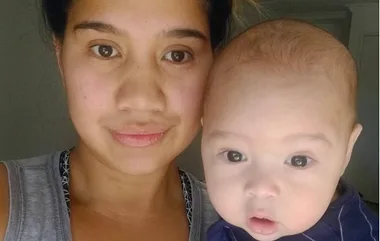 A woman holding a baby, both looking at the camera.