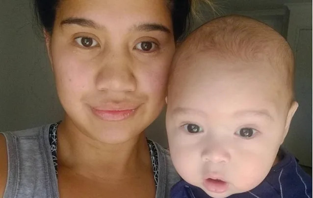A woman holding a baby, both looking at the camera.