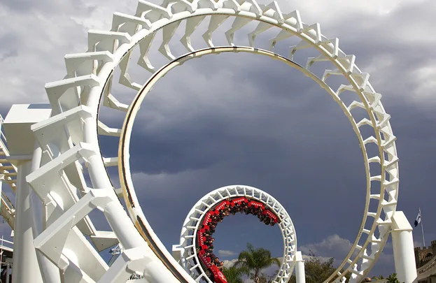 Roller coaster with a looping track against a cloudy sky, featuring a red train moving through the loops.