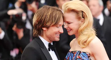 Two people in formal attire share a close, joyful moment on a red carpet, surrounded by photographers.