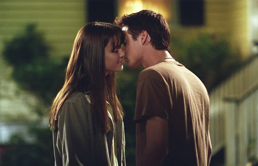Two people are leaning in for a kiss on a dimly lit outdoor setting.