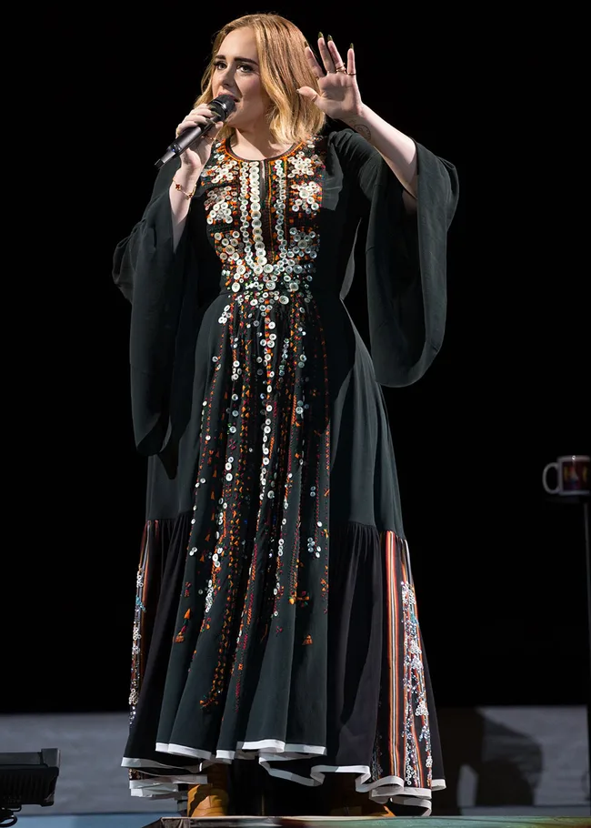 Singer performing on stage in a long black dress with colorful embellishments.