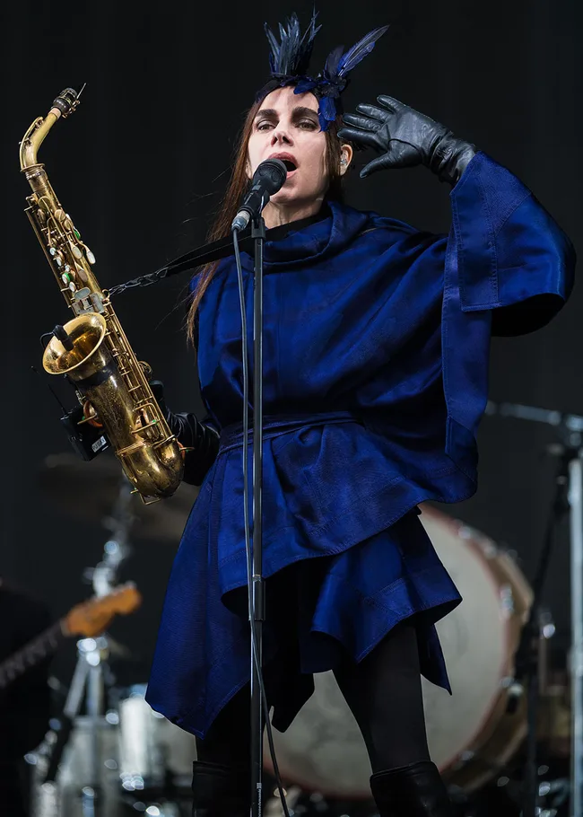 Singer in a blue outfit and feathered headpiece, holding a saxophone on stage.