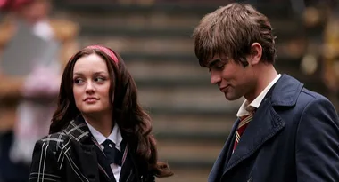 Two young adults in school uniforms stand together on outdoor steps, engaging in conversation.