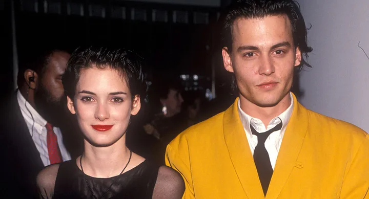 Two people posing together, one wearing a bright yellow jacket, at a formal event with a blurred crowd in the background.