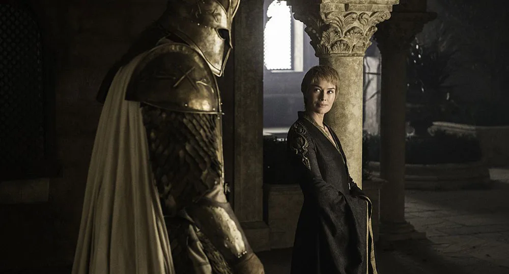 A woman in a dark dress stands beside a heavily armored knight in a dimly lit stone corridor.