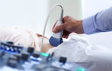 "Person receiving an abdominal ultrasound scan with a probe, medical equipment visible in the foreground."