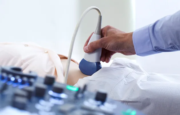 "Person receiving an abdominal ultrasound scan with a probe, medical equipment visible in the foreground."