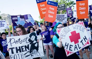 Pro-choice rally with participants holding signs like "Keep Clinics Open" and "Prioritize Women's Health."