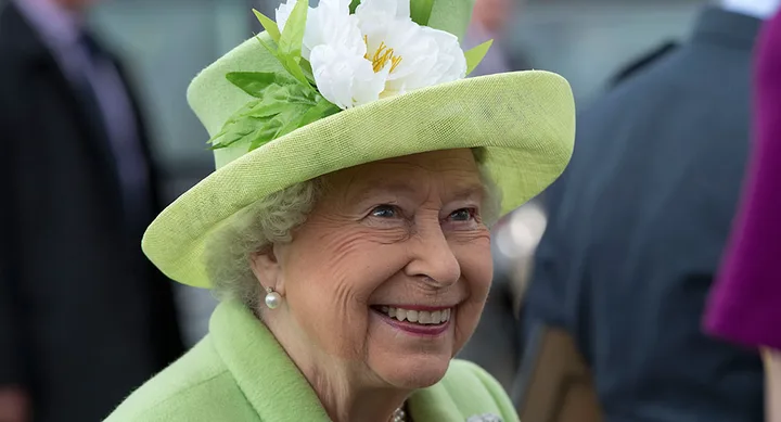Smiling elderly woman in a light green hat with a white flower, dressed in matching attire.