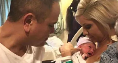 A man and a woman lovingly hold their newborn baby in a hospital room.