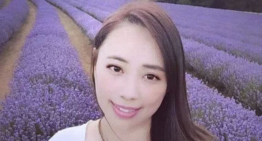 A woman smiling in a field of blooming lavender with rows of purple flowers behind her.