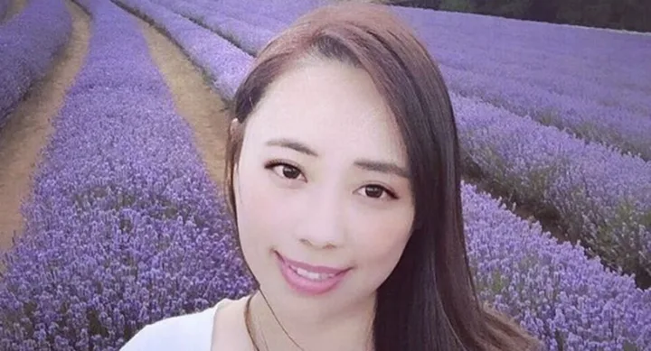 A woman smiling in a field of blooming lavender with rows of purple flowers behind her.