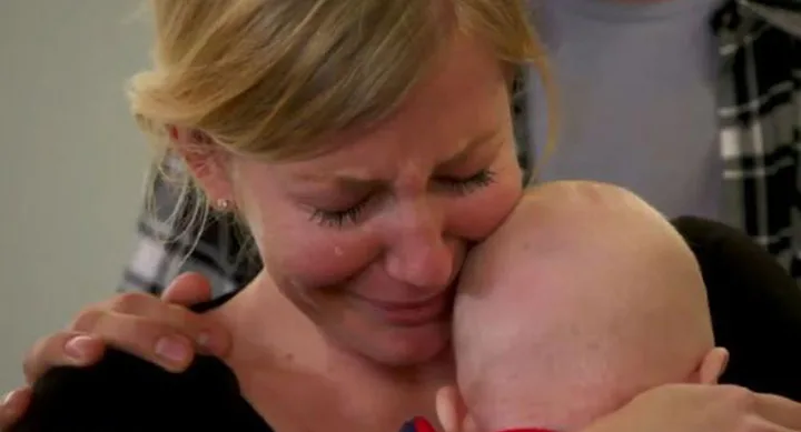 A woman cries while holding a baby close, with a comforting hand on her shoulder.