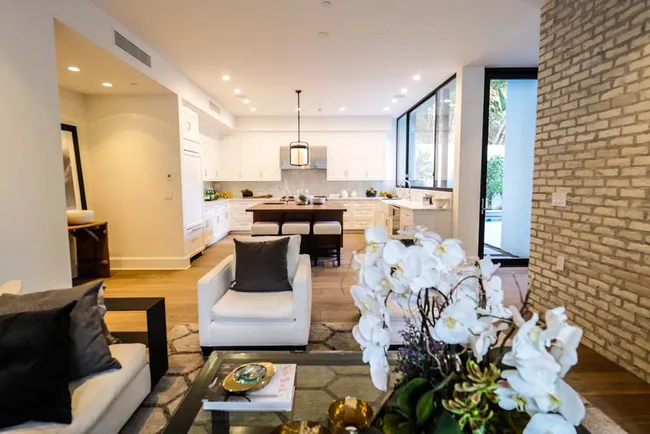 Modern open-concept living room and kitchen with white cabinets, pendant light, and brick accent wall.