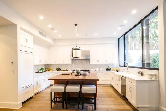 Modern kitchen with a central island, white cabinets, large windows, and recessed lighting.
