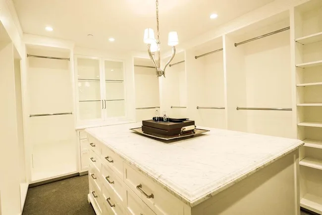 Luxurious, spacious walk-in closet with a marble-topped island, ample shelving, and soft lighting.