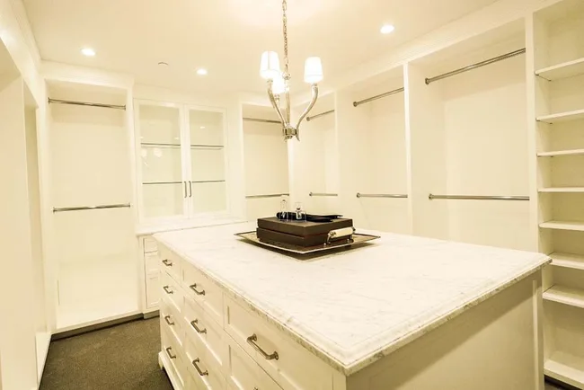 Luxurious, spacious walk-in closet with a marble-topped island, ample shelving, and soft lighting.