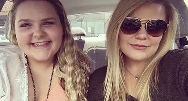 Two smiling women in a car, one with wavy hair, the other wearing sunglasses.