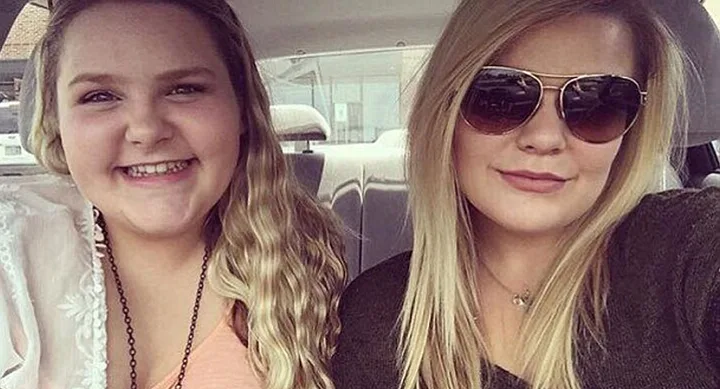 Two smiling women in a car, one with wavy hair, the other wearing sunglasses.