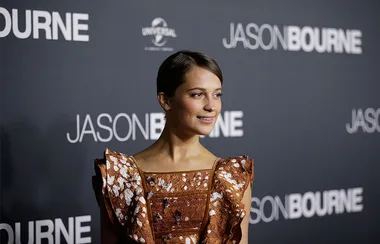 Actress at the "Jason Bourne" premiere, wearing a patterned brown dress, stands in front of a movie backdrop.