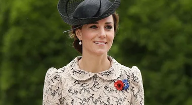 A woman in a lace dress and black hat with a poppy and blue flower brooch.