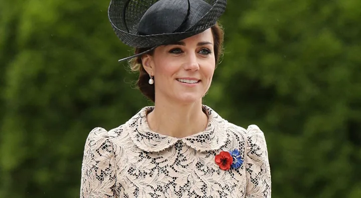 A woman in a lace dress and black hat with a poppy and blue flower brooch.