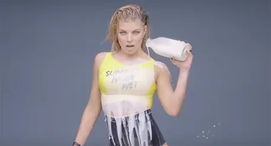 A person in a yellow top pouring milk on themselves with a serious expression.