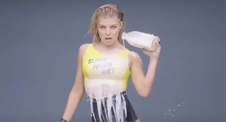 A person in a yellow top pouring milk on themselves with a serious expression.