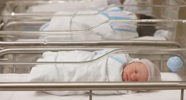 Newborn baby sleeping in a hospital bassinet, wrapped in a white blanket and wearing a striped beanie.