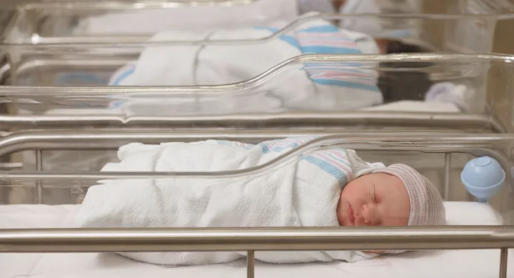 Newborn baby sleeping in a hospital bassinet, wrapped in a white blanket and wearing a striped beanie.