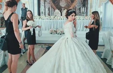 Bride in a white gown with a tiara, surrounded by three women in black dresses at a decorated wedding venue.