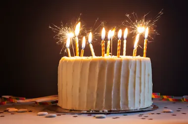 Birthday cake with lit candles and sparklers on top, set against a dark background.