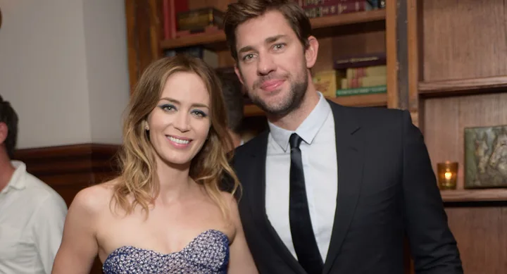 Young woman in a strapless dress and man in a suit smiling together at a formal event, with shelves and books in the background.