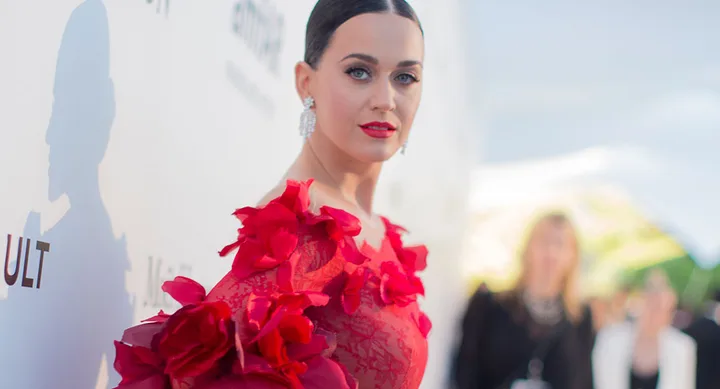 A person in a red floral dress poses at a formal event, with a blurred crowd in the background.