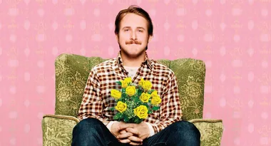 Man in plaid shirt sitting on a green chair holding a bouquet of yellow roses against a pink patterned background.