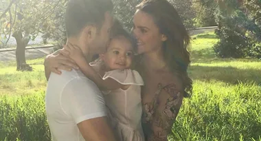 Family embracing in a sunlit park with lush green grass and trees in the background.
