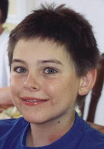 Young boy with short hair, smiling at the camera, wearing a blue shirt.