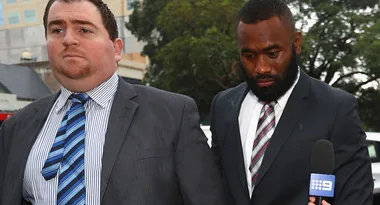 Two men in suits walking outside beside a microphone with a "9" logo.