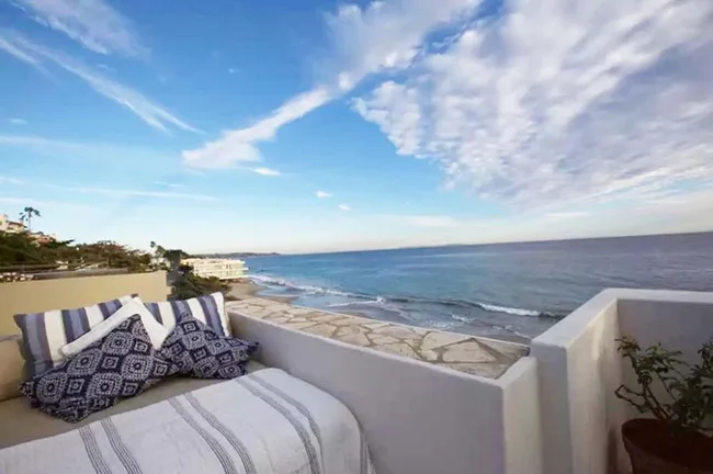 A cozy patio bed with blue pillows overlooks a scenic ocean view under a partly cloudy sky.