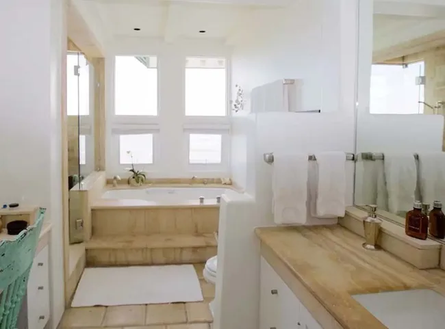 Bright bathroom with a large tub, wooden countertops, white towels, and three windows above the tub.