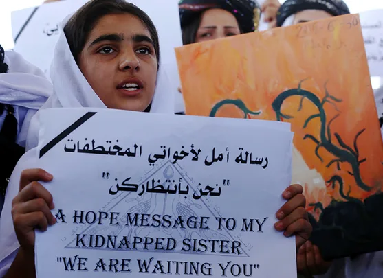 Young girl holding a sign reading "A hope message to my kidnapped sister 'We are waiting you'" in Arabic and English.