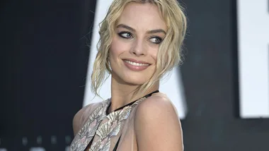 I don't know who this is, but it's a woman with blonde hair smiling at an event, wearing a dress with leaf designs.