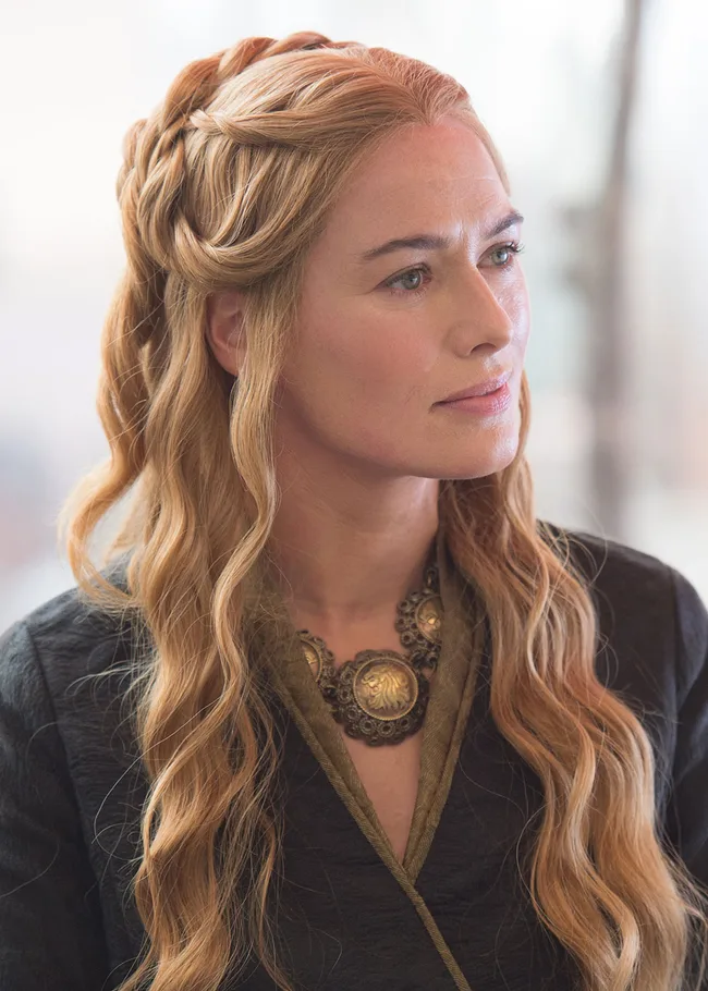 Portrait of a woman with long, wavy blonde hair, wearing a black cloak and ornate necklace, gazing to the side.